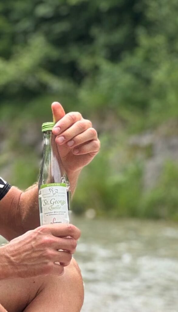 Läufer hält eine 0,33-Liter-Flasche St. Georgsquelel medium in Händen und sitzt am Bachufer