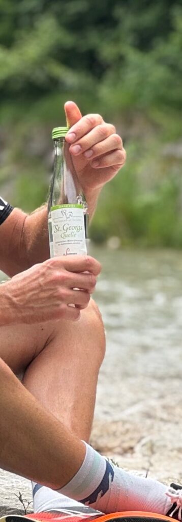 Läufer hält eine 0,33-Liter-Flasche St. Georgsquelel medium in Händen und sitzt am Bachufer